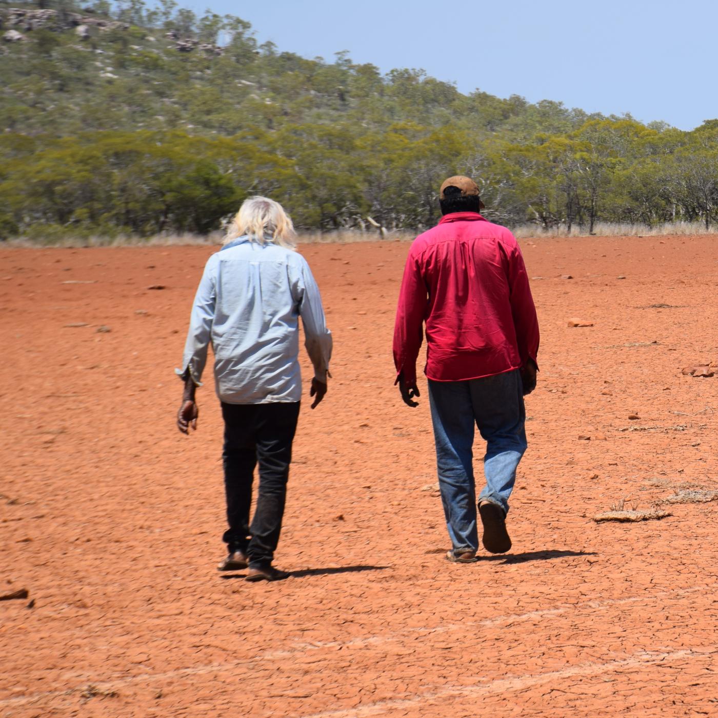 Two men walking across cracked dry red mud flat